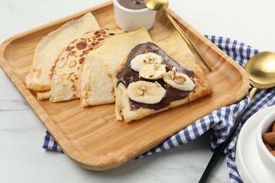 Delicious crepes with chocolate sauce, banana and almonds served on white marble table, closeup