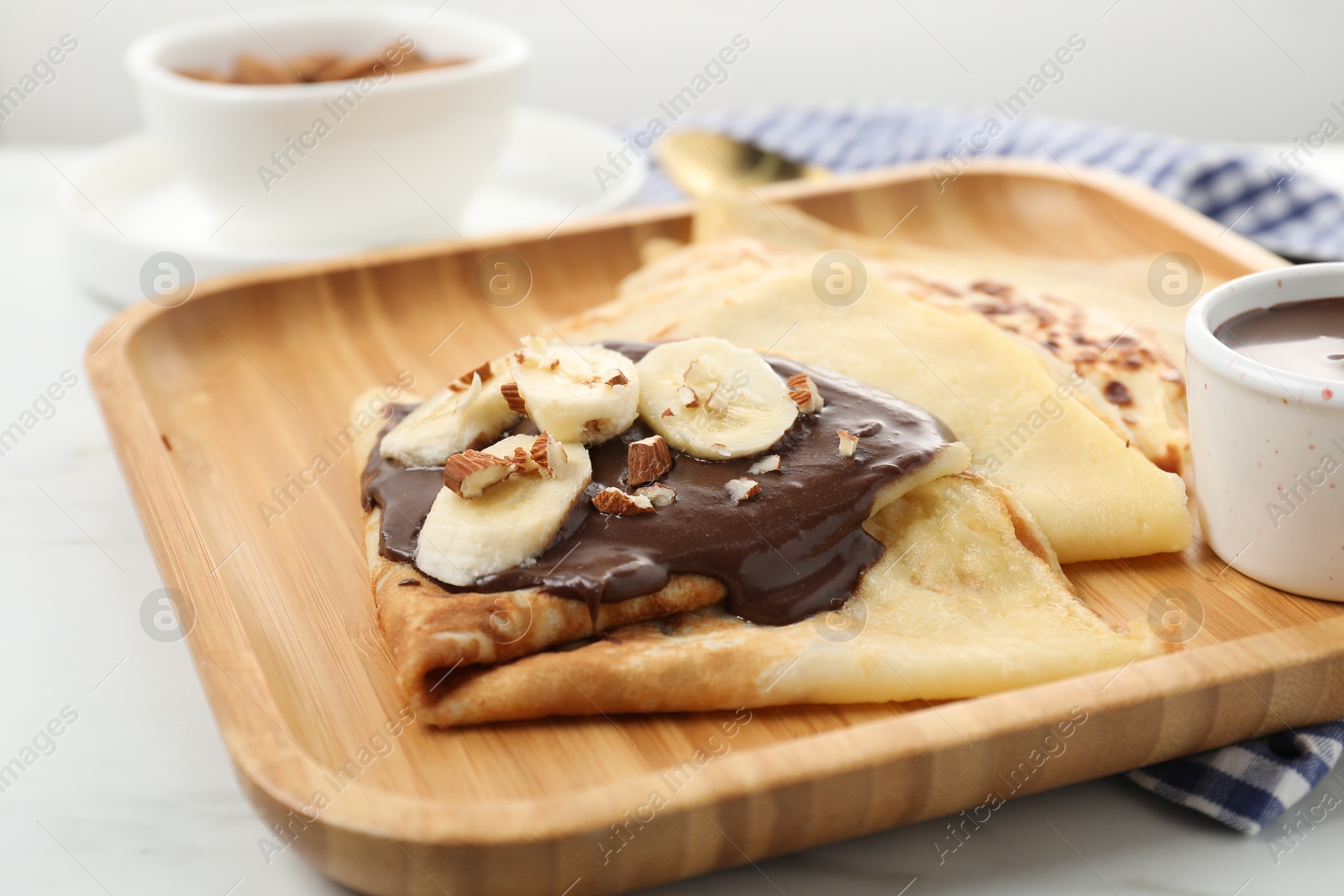 Photo of Delicious crepes with chocolate sauce, banana and almonds on white table, closeup