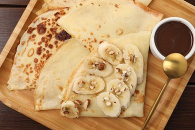 Delicious crepes with chocolate sauce, banana and almonds on wooden table, top view