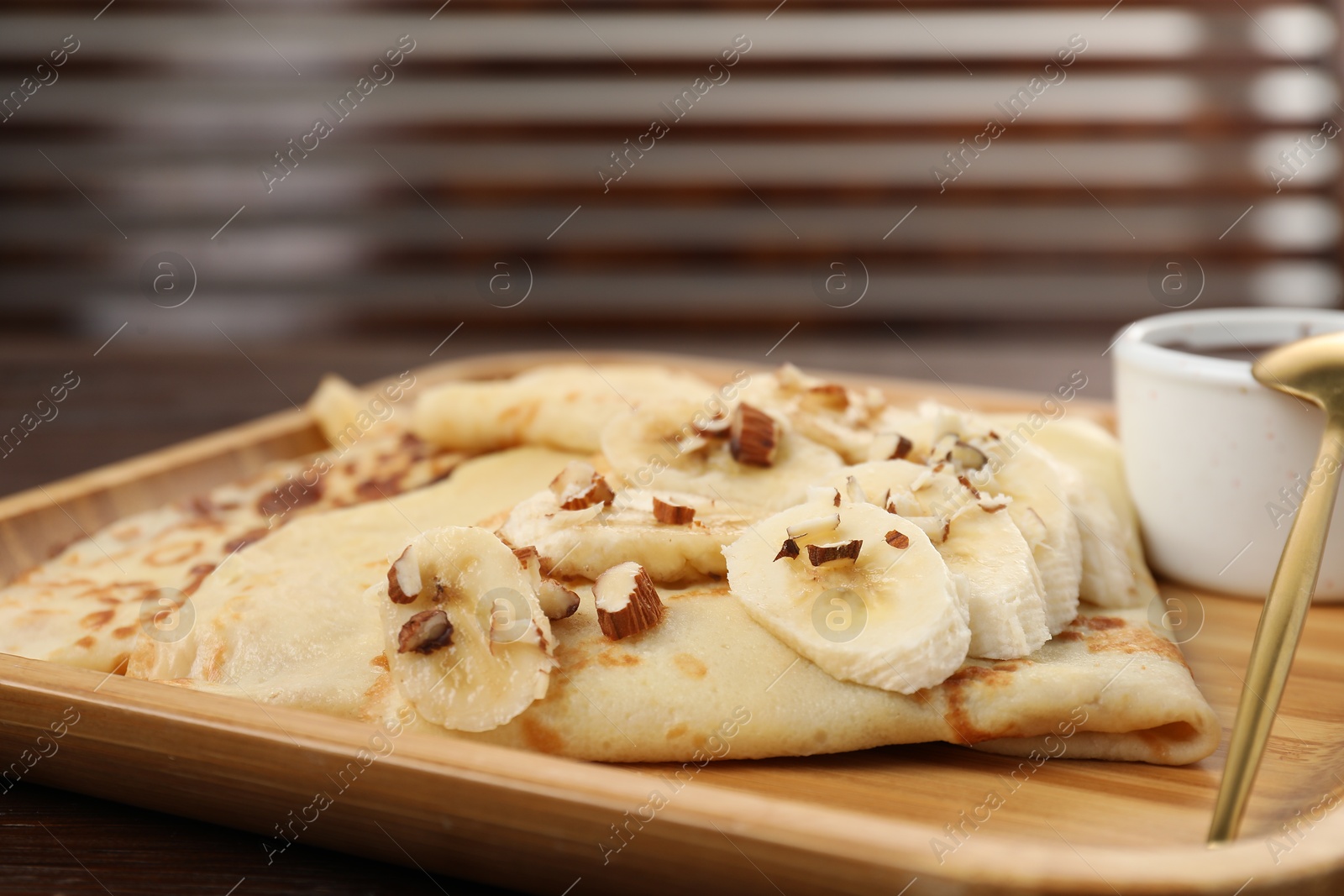 Photo of Delicious crepes with chocolate sauce, banana and almonds on wooden table, closeup