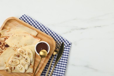 Photo of Delicious crepes with chocolate sauce, banana and almonds on white marble table, top view. Space for text