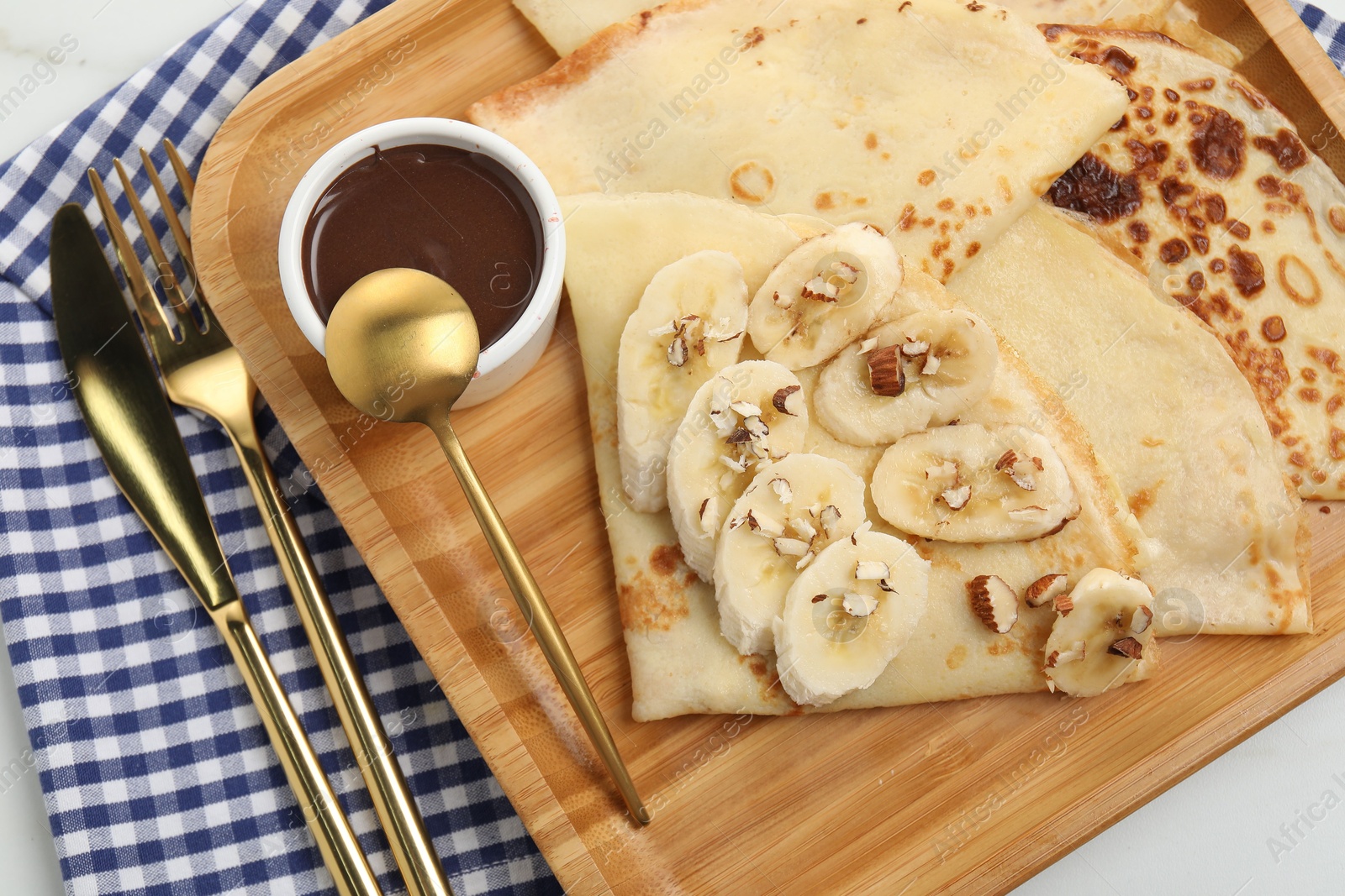 Photo of Delicious crepes with chocolate sauce, banana and almonds on white table, top view