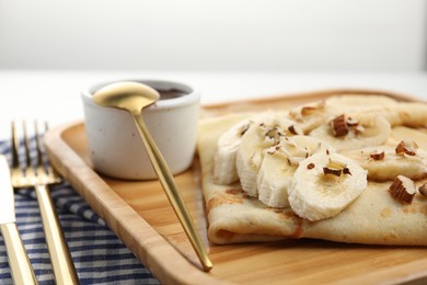 Photo of Delicious crepes with chocolate sauce, banana and almonds on white table, closeup