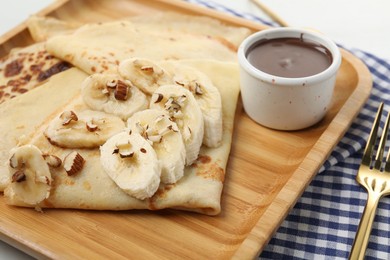 Photo of Delicious crepes with chocolate sauce, banana and almonds on table, closeup