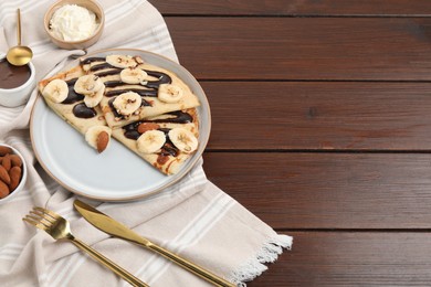 Delicious crepes with chocolate sauce, banana and almonds served on wooden table. Space for text