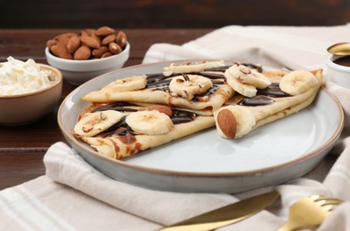 Photo of Delicious crepes with chocolate sauce, banana and almonds served on wooden table, closeup