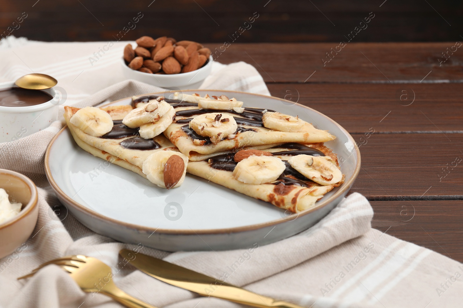 Photo of Delicious crepes with chocolate sauce, banana and almonds served on wooden table, closeup