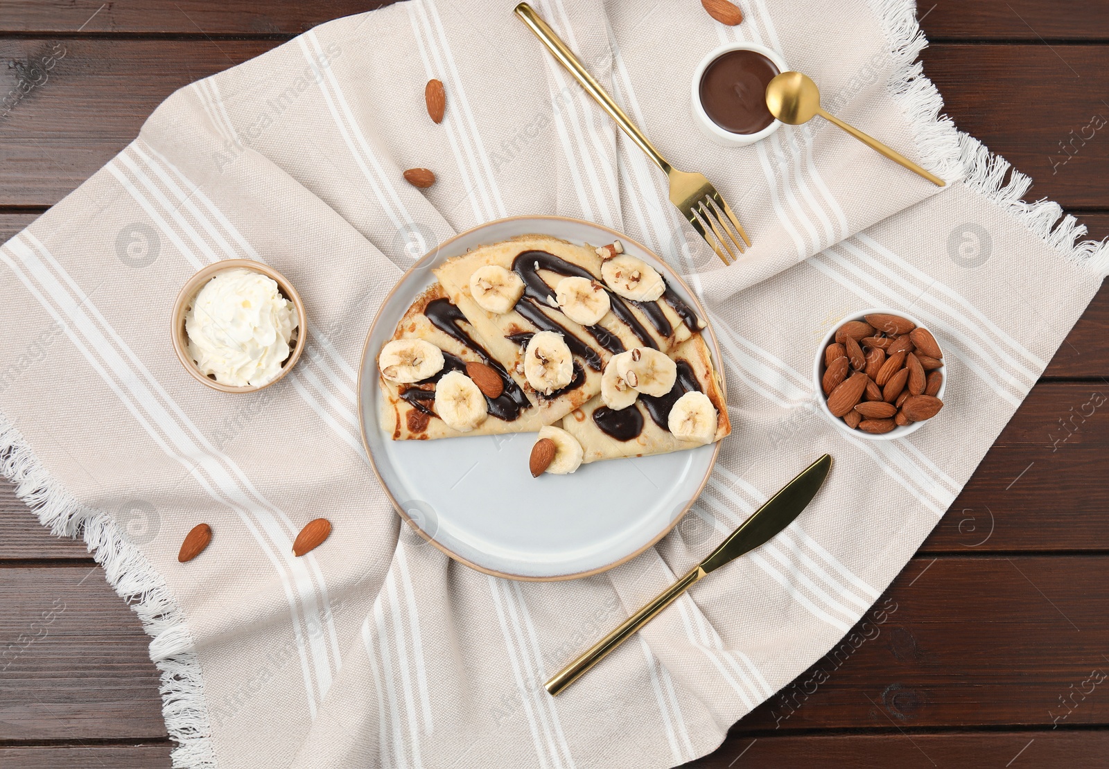 Photo of Delicious crepes with chocolate sauce, banana and almonds served on wooden table, flat lay