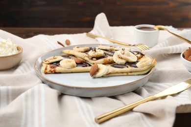 Photo of Delicious crepes with chocolate sauce, banana and almonds served on table