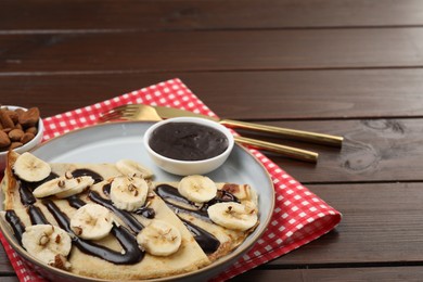 Photo of Delicious crepes with chocolate sauce, banana and almonds served on wooden table. Space for text