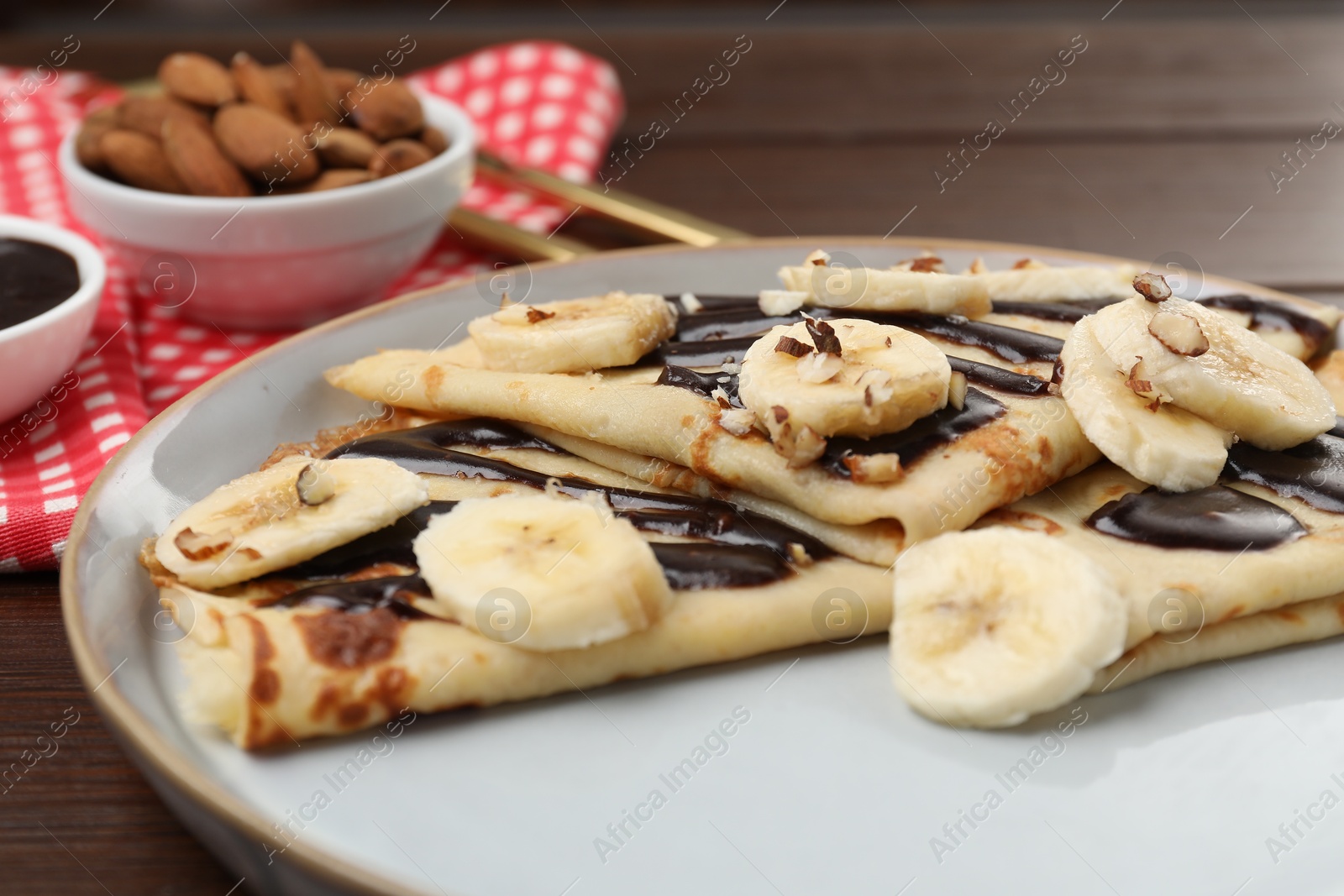 Photo of Delicious crepes with chocolate sauce, banana and almonds served on wooden table, closeup