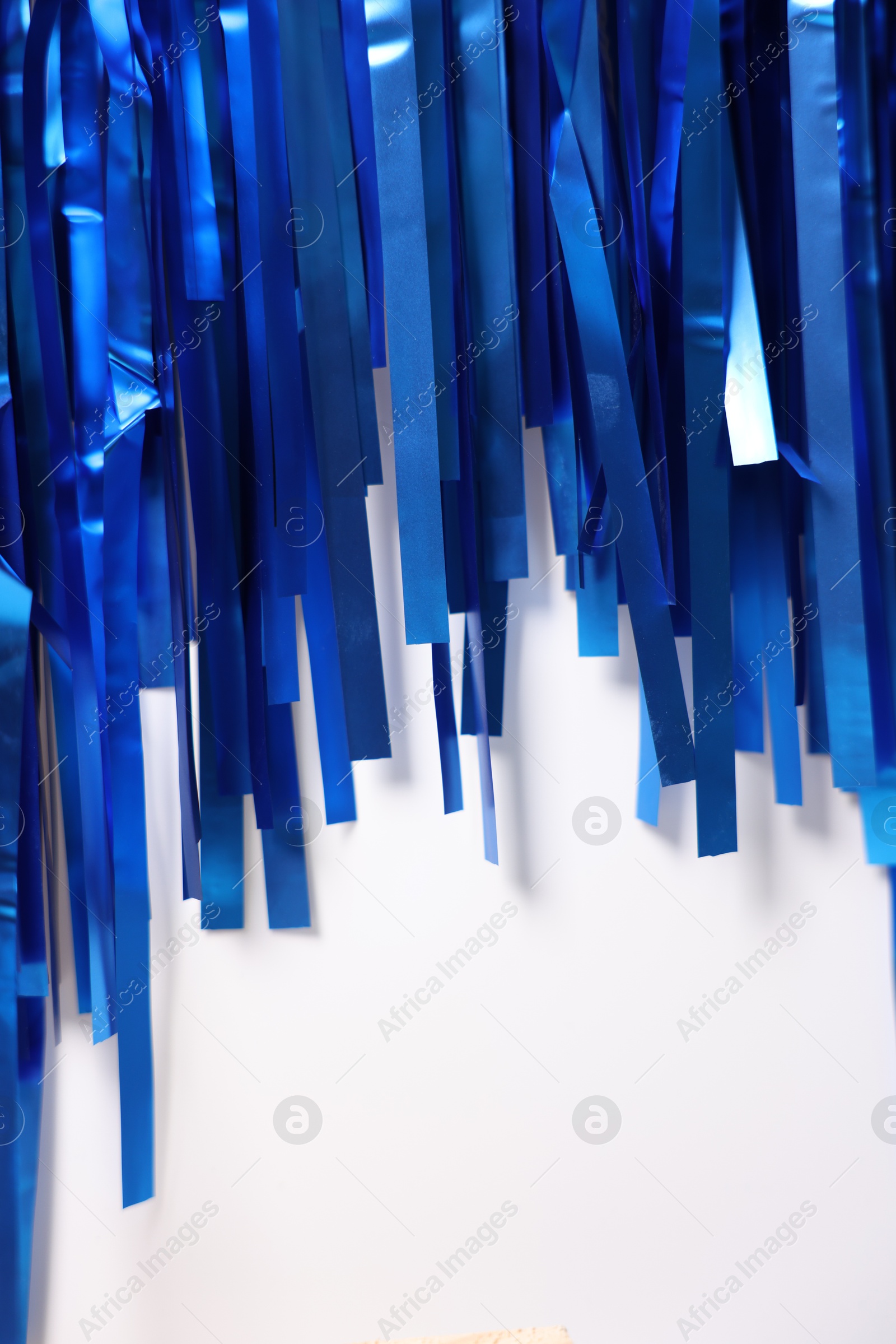 Photo of Shiny blue foil curtain on white background, closeup