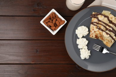 Photo of Delicious crepes with banana, chocolate sauce and whipped cream served on wooden table, top view. Space for text