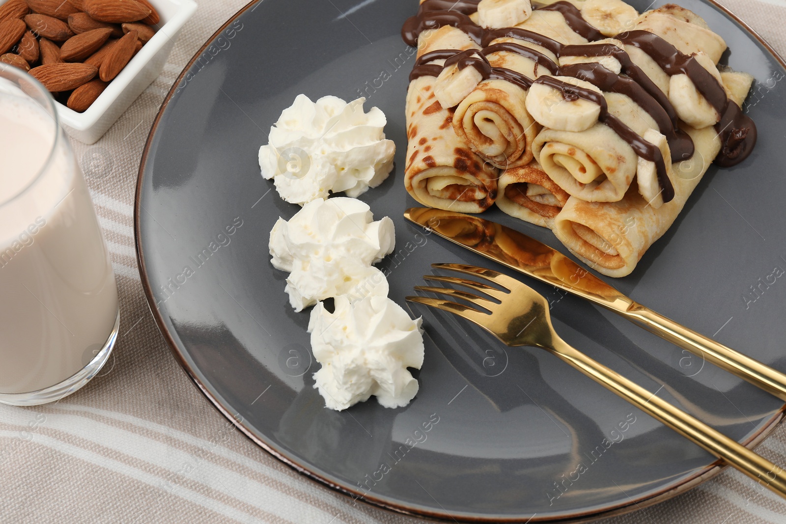 Photo of Delicious crepes with banana, chocolate sauce and whipped cream served on table, closeup