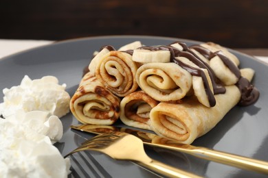 Photo of Delicious crepes with chocolate sauce, banana and whipped cream on plate, closeup