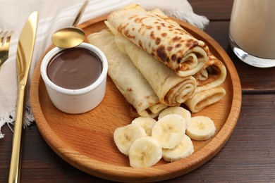 Delicious crepes served with chocolate sauce and banana on wooden table, closeup