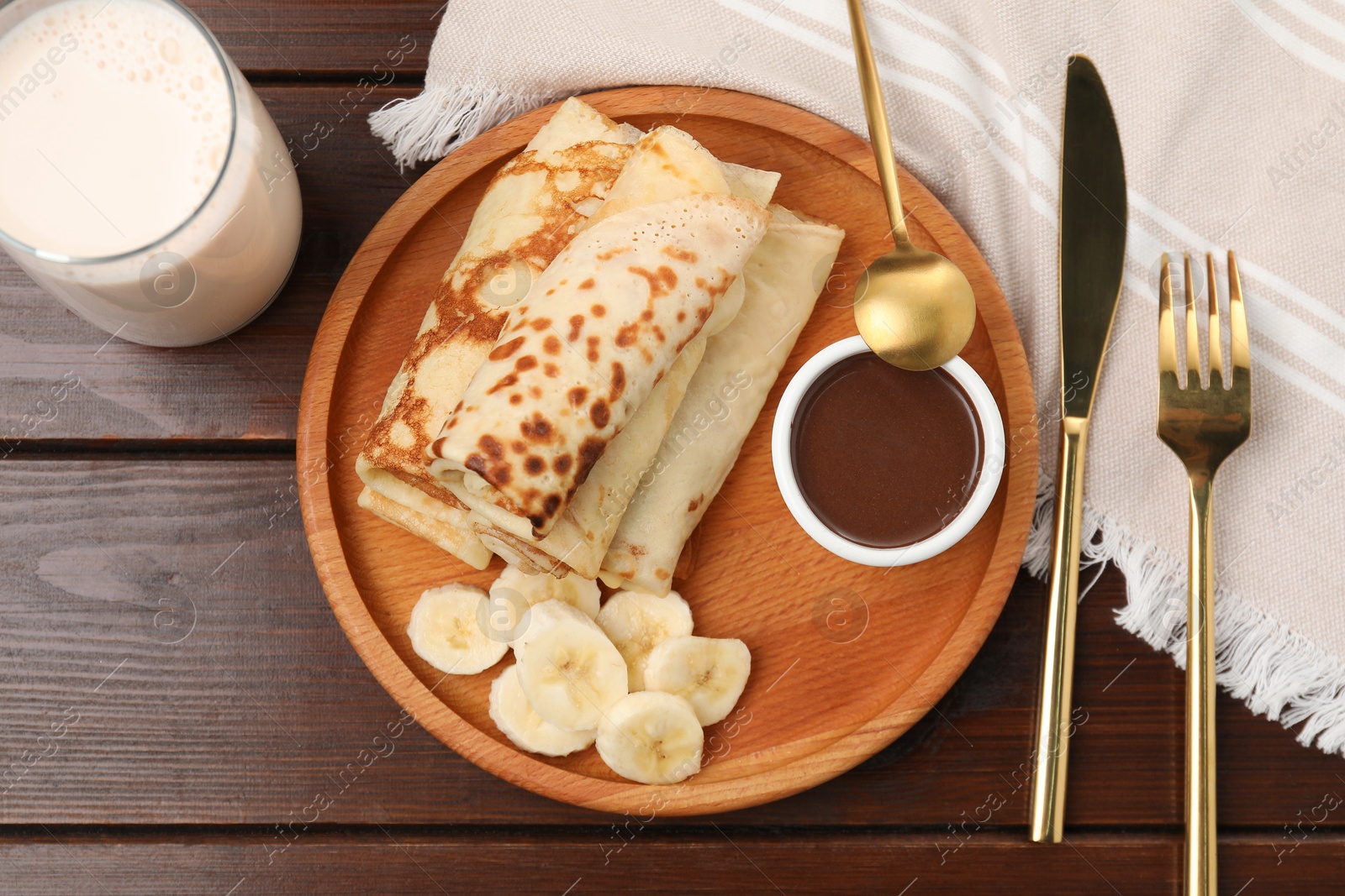 Photo of Delicious crepes served with chocolate sauce and banana on wooden table, flat lay