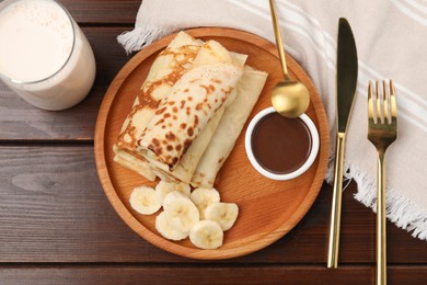 Photo of Delicious crepes served with chocolate sauce and banana on wooden table, flat lay