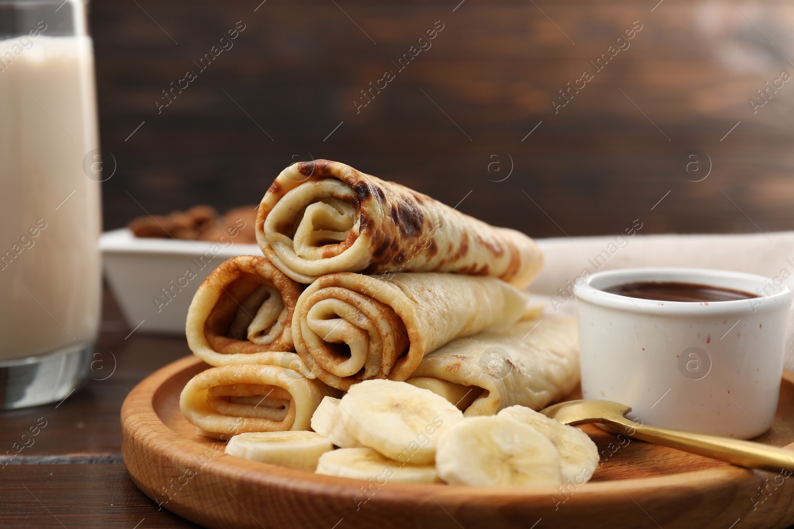 Photo of Delicious crepes served with chocolate sauce and banana on wooden table, closeup