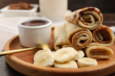 Delicious crepes served with chocolate sauce and banana on wooden table, closeup