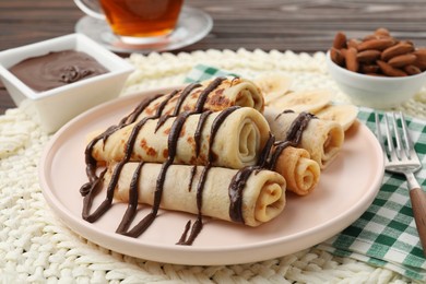 Photo of Delicious crepes with chocolate sauce and banana served on table, closeup