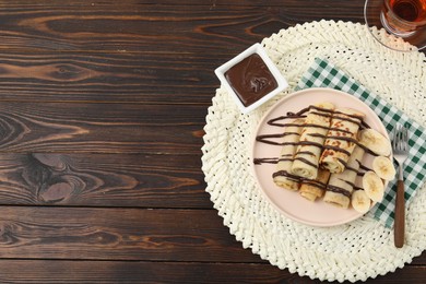 Photo of Delicious crepes with chocolate sauce and banana served on wooden table, top view. Space for text