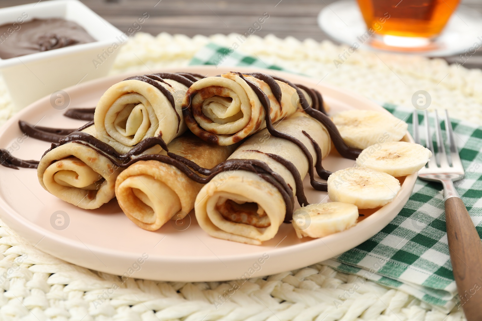 Photo of Delicious crepes with chocolate sauce and banana served on table, closeup