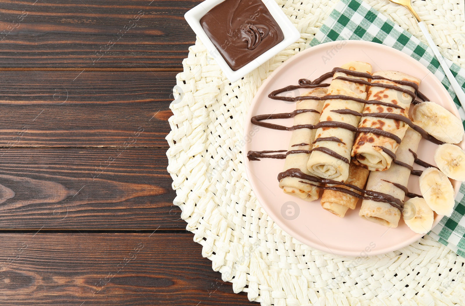 Photo of Delicious crepes with chocolate sauce and banana served on wooden table, top view. Space for text