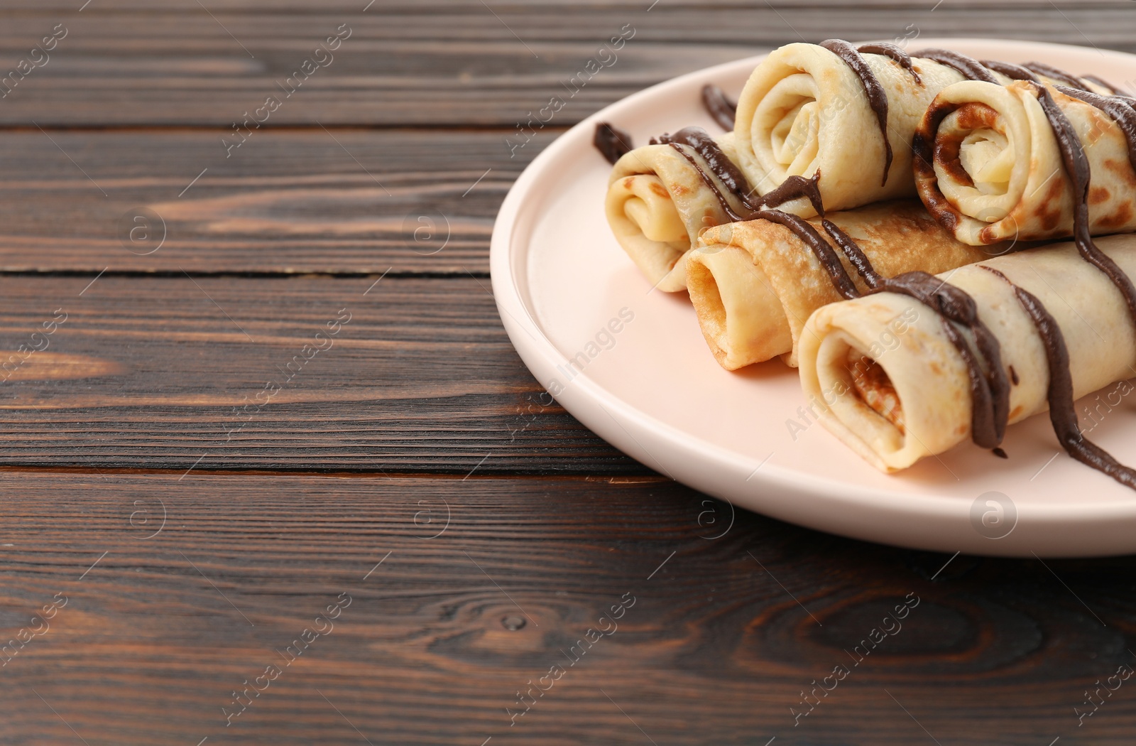 Photo of Delicious crepes with chocolate sauce on wooden table, closeup. Space for text