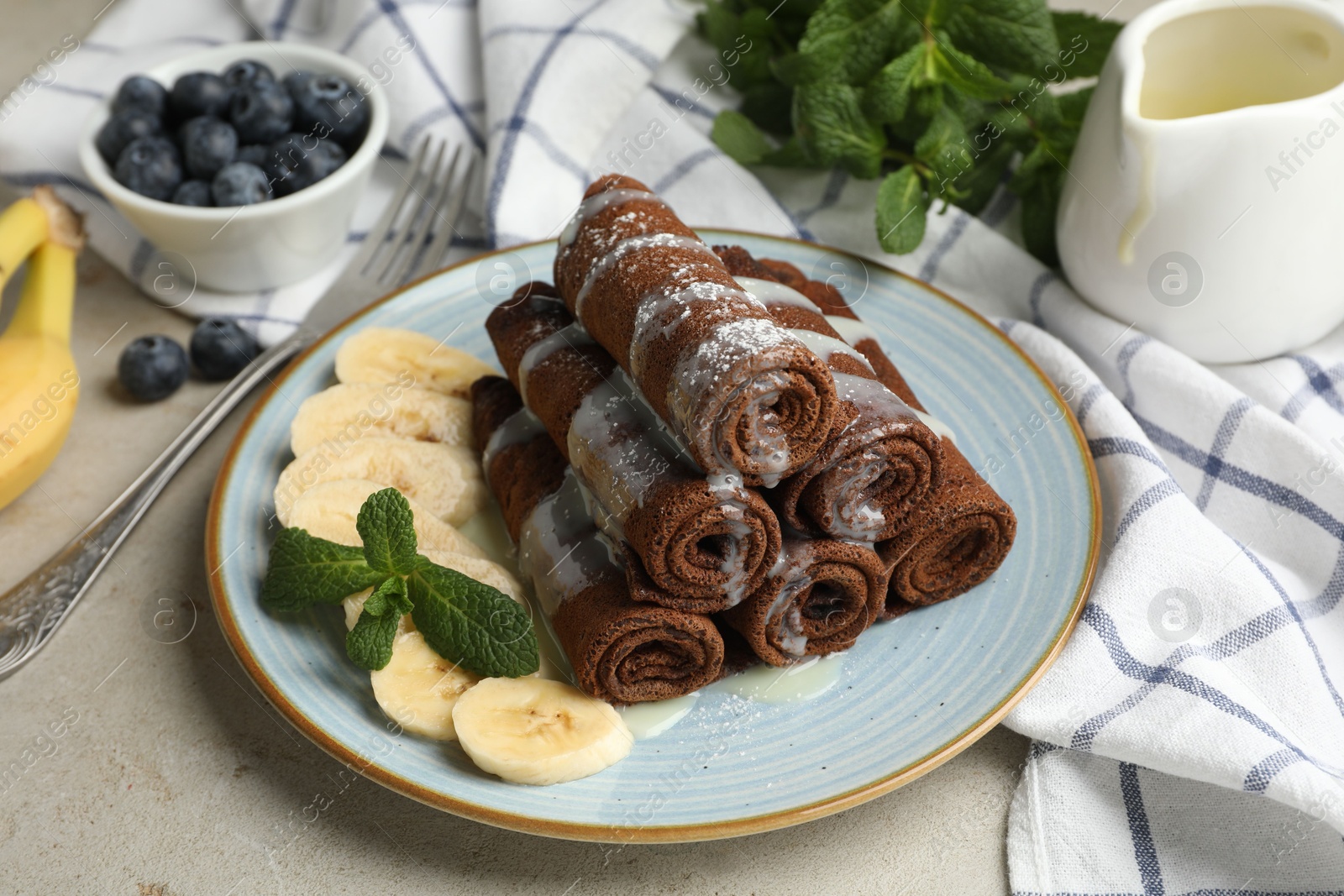 Photo of Delicious chocolate crepes with banana and blueberries served on light table, closeup