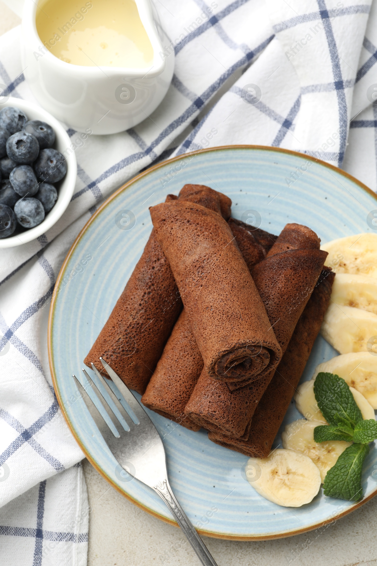 Photo of Delicious chocolate crepes with banana and blueberries served on light table, flat lay