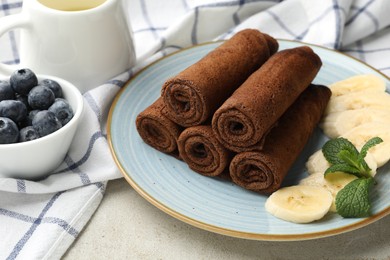 Photo of Delicious chocolate crepes with banana and blueberries served on light table, closeup