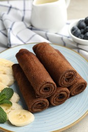 Photo of Delicious chocolate crepes with banana and blueberries served on light table, closeup