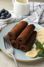 Photo of Delicious chocolate crepes with banana and blueberries served on light table, closeup