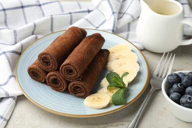 Photo of Delicious chocolate crepes with banana and blueberries served on light table, closeup