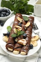 Photo of Delicious chocolate crepes with banana and blueberries served on white marble table, closeup