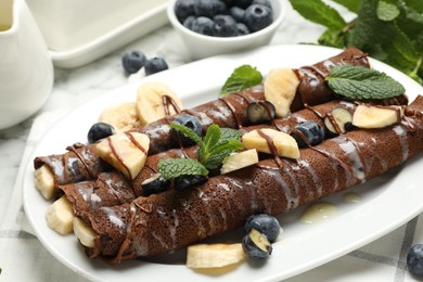 Photo of Delicious chocolate crepes with banana and blueberries served on white marble table, closeup