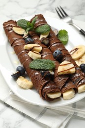 Photo of Delicious chocolate crepes with banana and blueberries served on white marble table, closeup