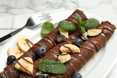 Photo of Delicious chocolate crepes with banana and blueberries served on white marble table, closeup