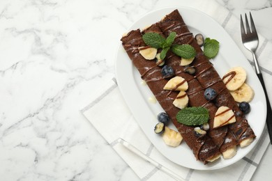 Photo of Delicious chocolate crepes with banana and blueberries served on white marble table, top view. Space for text