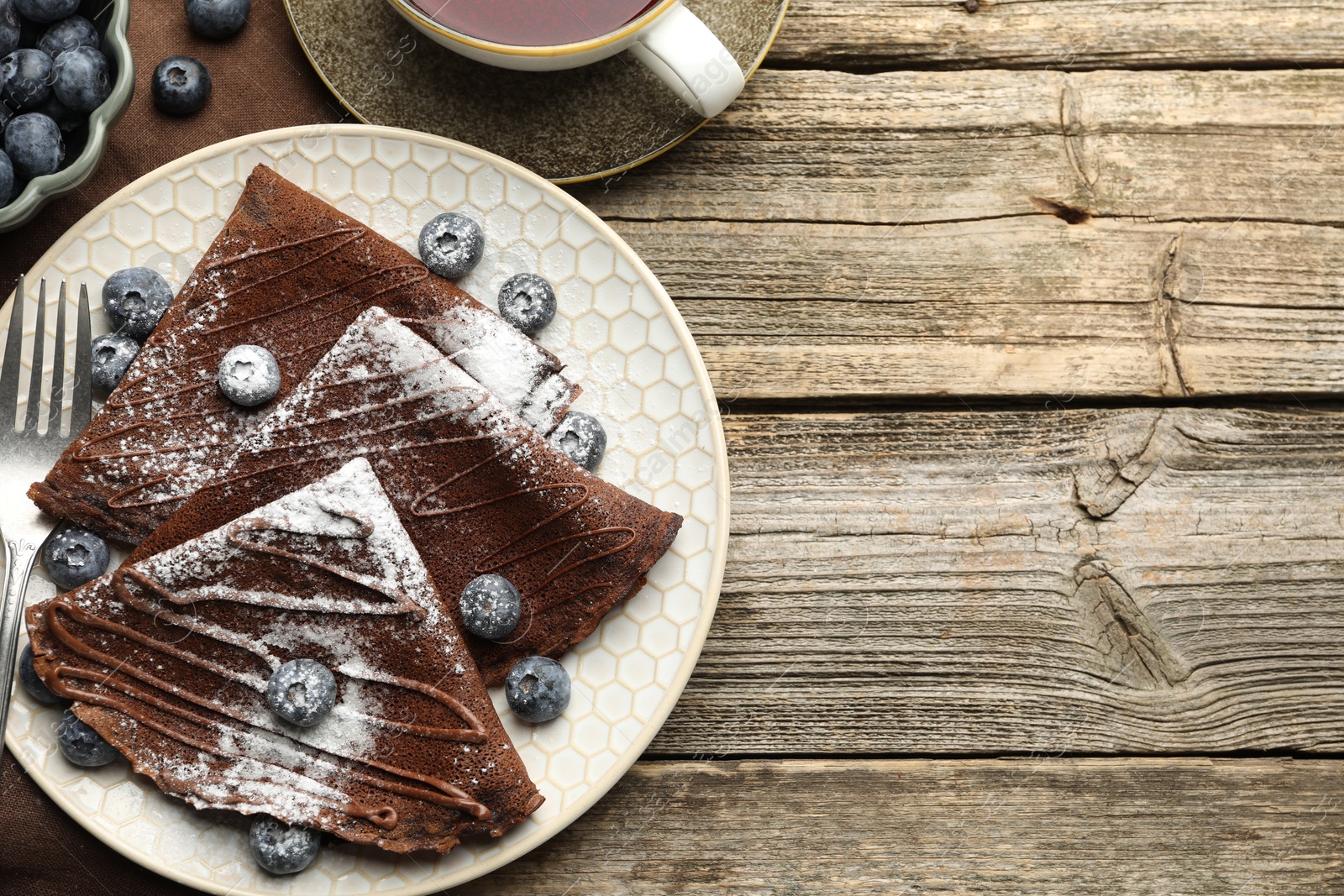 Photo of Delicious chocolate crepes with blueberries served on wooden table, flat lay. Space for text