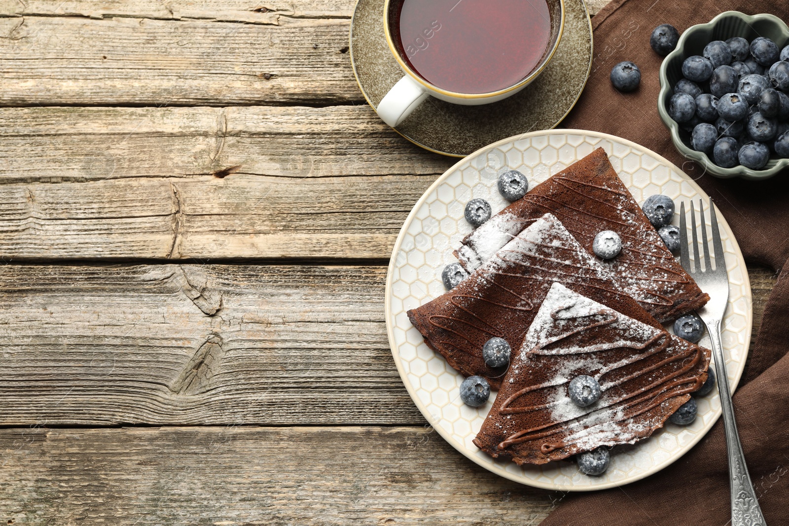 Photo of Delicious chocolate crepes with blueberries served on wooden table, flat lay. Space for text