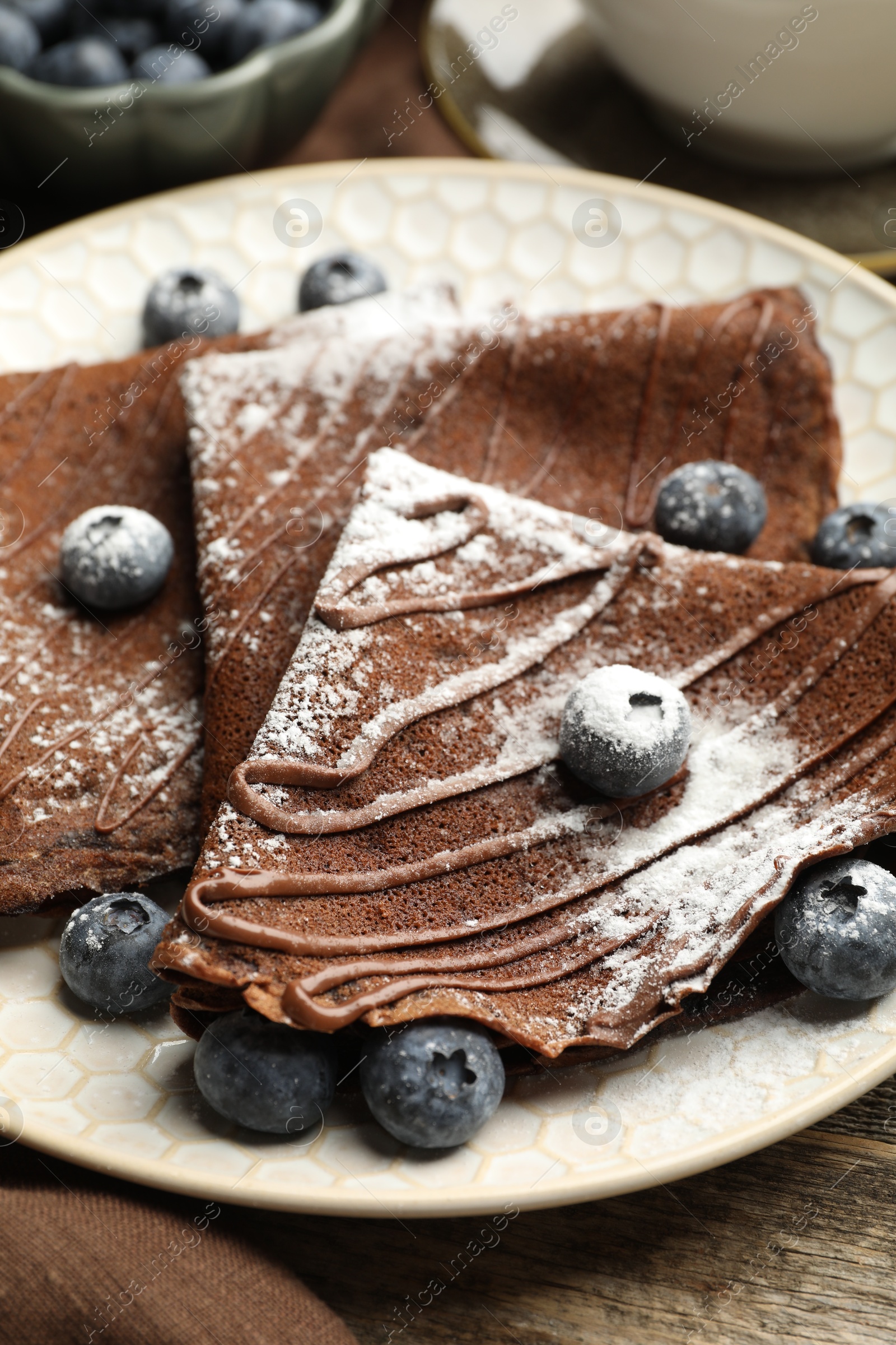 Photo of Delicious chocolate crepes with blueberries served on wooden table, closeup