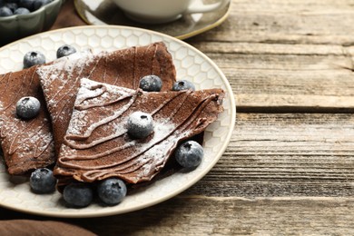 Photo of Delicious chocolate crepes with blueberries served on wooden table, closeup. Space for text