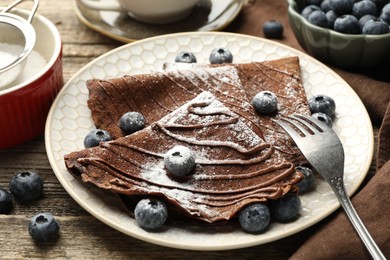 Photo of Delicious chocolate crepes with blueberries served on wooden table, closeup