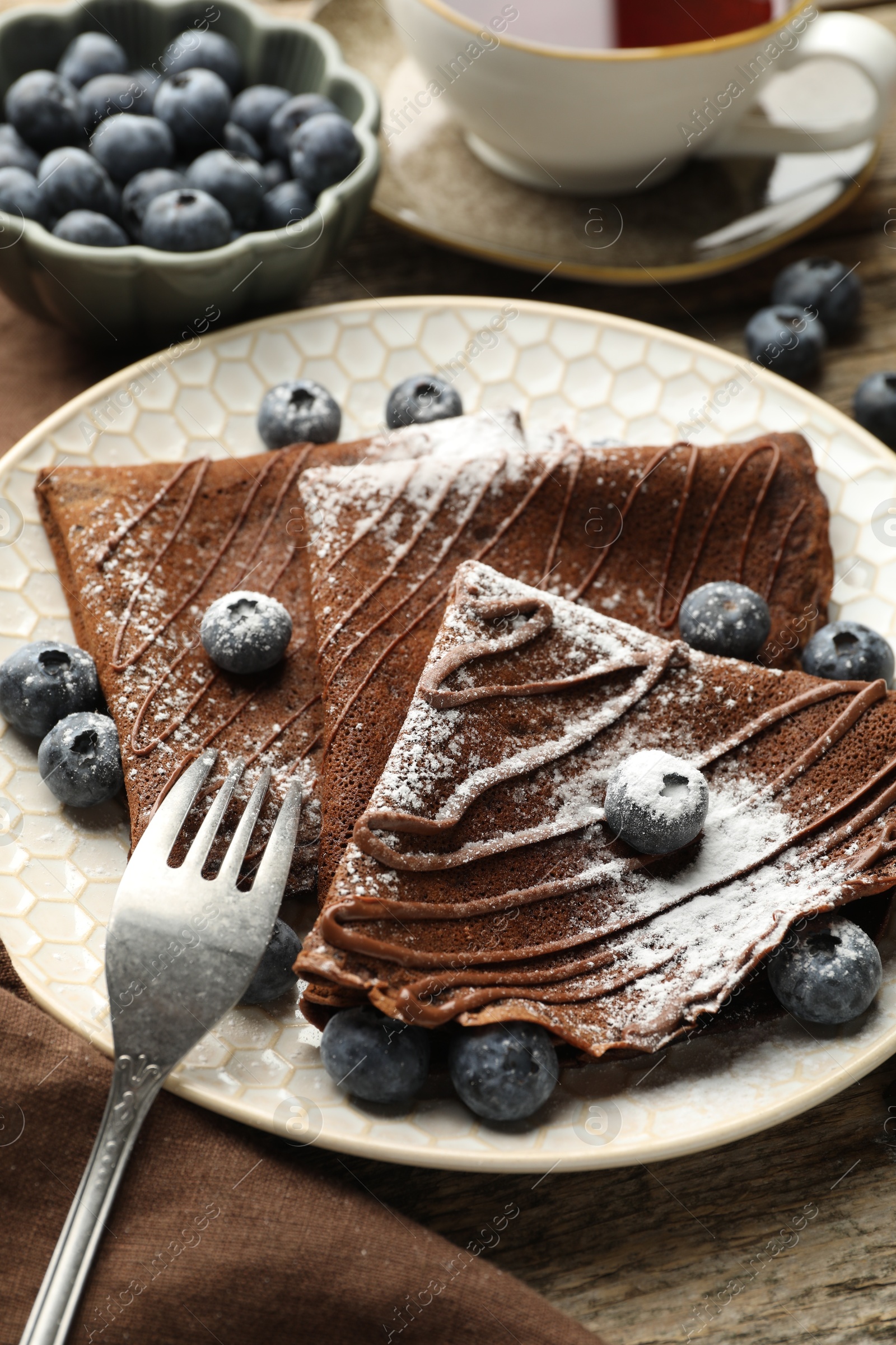 Photo of Delicious chocolate crepes with blueberries served on wooden table, closeup