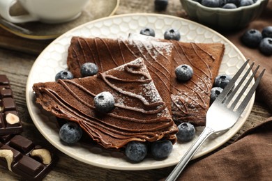 Photo of Delicious chocolate crepes with blueberries served on wooden table, closeup