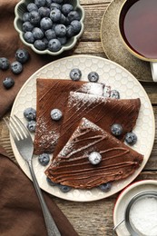 Photo of Delicious chocolate crepes with blueberries served on wooden table, flat lay