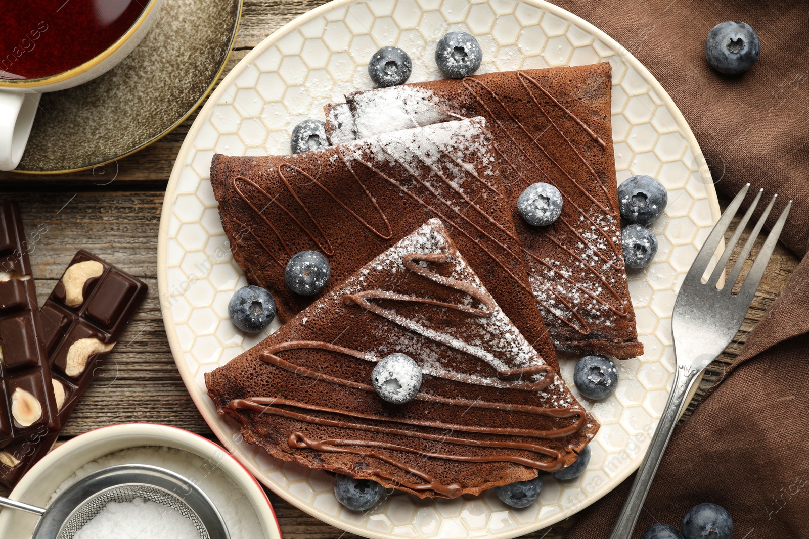 Photo of Delicious chocolate crepes with blueberries served on wooden table, flat lay