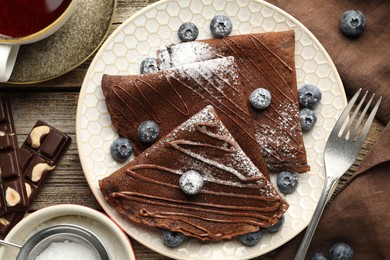 Photo of Delicious chocolate crepes with blueberries served on wooden table, flat lay